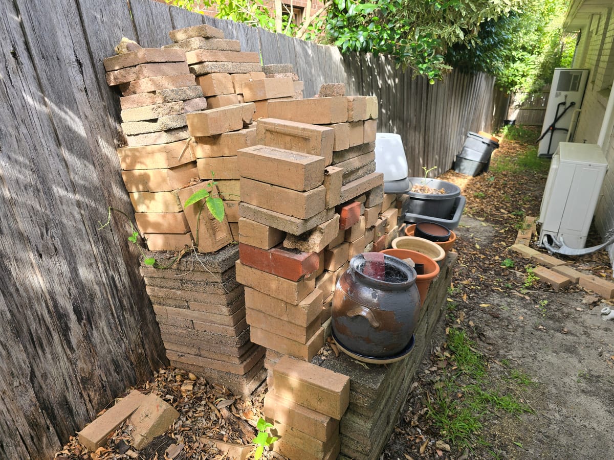 Pile of bricks and pavers stacked in a side yard before construction waste removal in Melbourne